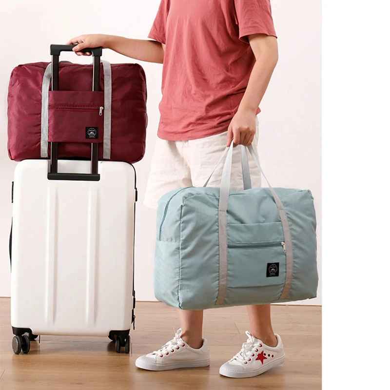 Foldable travel duffel bags in blue and red with dual carry handles, front zip pockets, and a trolley sleeve that fits over a suitcase handle for convenient travel.