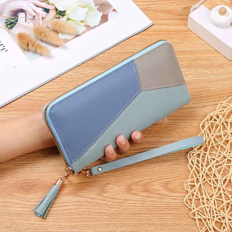 Blue women's patchwork zip wallet with tassel zipper pull in hand